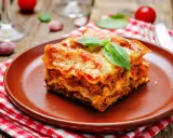 Une part généreuse de lasagne végétarienne, dorée au four, garnie de basilic frais, sur une assiette en terre cuite.