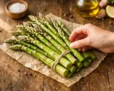 Un bouquet d'asperges vertes fraîches, prêt pour une délicieuse recette. Huile d'olive, citron et ail en arrière-plan.