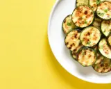 Courgettes rondes grillées à l'air fryer, parsemées d'herbes fraîches, sur une assiette blanche, sur fond jaune vif.