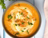 Un bol de soupe crémeuse aux lentilles corail, garni de crème et de persil frais, prêt à être dégusté avec une cuillère.
