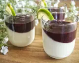 Trois panna cotta crémeuses, garnies d'un coulis pour panna cotta aux fruits rouges et d'une tranche de citron vert, sur un fond de fleurs blanches.