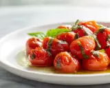 Tomates cerises confites, une recette simple et savoureuse, garnies de basilic frais sur une assiette blanche.