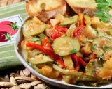Un plat de légumes mijotés, rappelant un pisto manchego, avec des courgettes, poivrons et tomates, servi avec des toasts grillés.