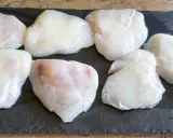 Plusieurs morceaux de lotte crue, prêts pour une cuisson au four, sont disposés sur une planche d'ardoise.