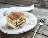 Une part de tiramisu maison, saupoudrée de cacao, sur une assiette blanche, prête à être dégustée. La conservation de ce délice est essentielle pour en savourer chaque bouchée.