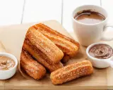 Churros dorés et croustillants, saupoudrés de sucre, prêts à être trempés dans le chocolat. Une recette gourmande pour un goûter parfait.