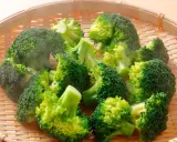 Brocolis coupés en bouquets dans un panier en osier, prêts pour la cuisson. La vapeur s'échappe, signe d'une cuisson à la vapeur parfaite.