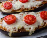 Deux aubergines farcies, garnies de tomates et de fromage fondu, prêtes à être dégustées.