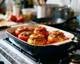 Cinq tomates farcies à la viande, prêtes pour le temps de cuisson. Elles reposent dans un plat allant au four sur une cuisinière.