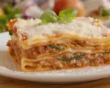 Une part généreuse de lasagne sans béchamel, avec sa garniture savoureuse et sa touche de crème fraîche, est saupoudrée de parmesan et décorée de basilic frais.