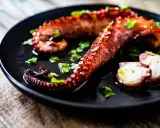 Tentacules de poulpe grillés, parsemés de persil frais, prêts à être dégustés. Une recette poulpe simple et savoureuse.