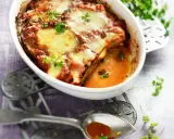 Un plat de recette parmigiana napolitaine gratinée, avec des aubergines, de la sauce tomate et du fromage fondant, garni de persil frais.