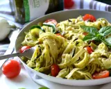 Un plat de tagliatelles de courgettes, tomates cerises et pesto, garni de basilic frais et de pignons de pin.