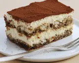 Une part de tiramisu sans oeuf, légère et aérienne, saupoudrée de cacao, sur une assiette blanche avec une fourchette.