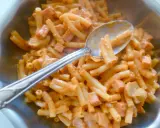Une cuillère sert une généreuse portion de timbale milanaise crémeuse, avec des pâtes courtes et des morceaux de jambon.