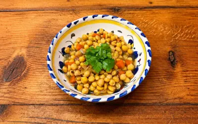 Un plat de pois chiches cuisinés avec des carottes et des oignons, garni de coriandre fraîche. La cuisson pois chiche est réussie, le plat est appétissant.