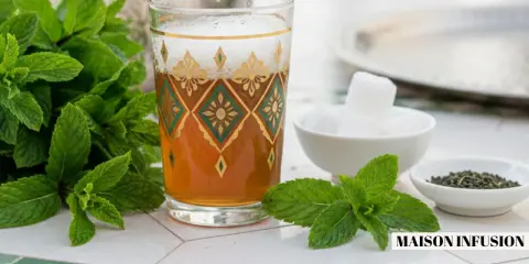 Un verre orné de motifs dorés et verts contient du thé marocain, accompagné de menthe fraîche, de sucre en morceaux et de feuilles de thé.