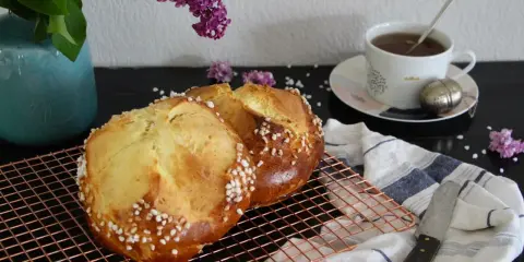 Deux pains briochés, parfaits pour une mouna recette, refroidissent sur une grille. Une tasse de thé et des lilas complètent la scène.