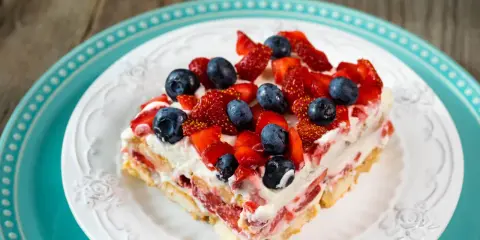 Tranche de tiramisu aux fruits rouges, garnie de fraises et myrtilles fraîches, sur une assiette blanche ornée.