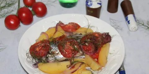 Maquereau au vin blanc, pommes de terre, tomates et oignons sur une assiette blanche.
