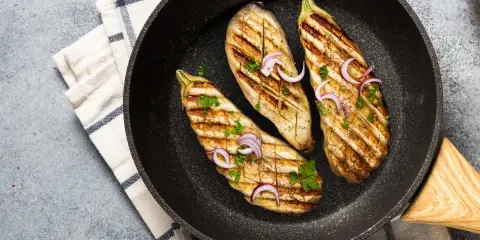 Aubergines grillées dans une poêle, garnies d'oignons rouges et de persil. Une délicieuse recette aubergine prête à être dégustée.