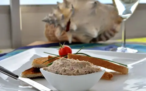 Un bol de rillettes de maquereau, servi avec des toasts grillés, une tomate cerise et un verre de vin blanc.