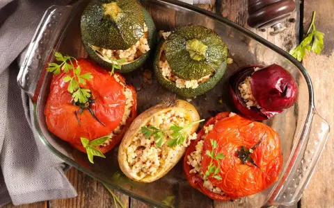 Plat de farce à légume : tomates, courgettes rondes, oignon rouge et pomme de terre farcis de grains, joliment présentés dans un plat en verre.