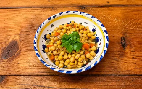 Un plat de pois chiches cuisinés avec des carottes et des oignons, garni de coriandre fraîche. La cuisson pois chiche est réussie, le plat est appétissant.