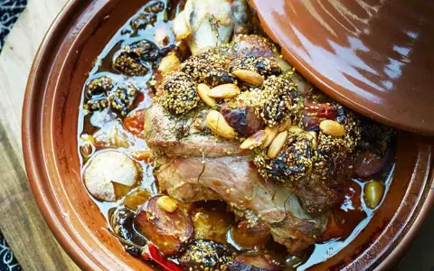 Un plat de tajine agneau aux pruneaux, amandes et sésame, mijotant dans sa sauce parfumée.