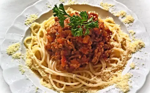 Une assiette de spaghetti bolognaise italienne, garnie de persil frais et de parmesan râpé. Un délice pour les amateurs de cuisine italienne.