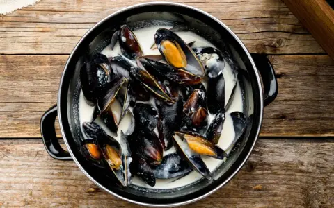 Un plat de moules à la crème, prêtes à être dégustées, sur une table en bois rustique.