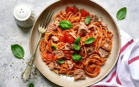 Assiette de pâtes au thon, sauce tomate et basilic frais. Un plat simple et savoureux prêt à être dégusté.
