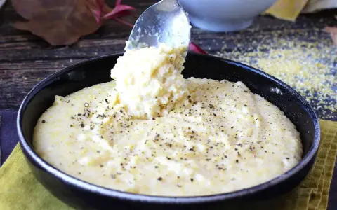 Une cuillère sert une portion généreuse de polenta crémeuse, assaisonnée de poivre noir, dans un bol. Une recette polenta réconfortante.