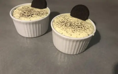 Deux ramequins de tiramisu Oreo, saupoudrés de miettes de biscuit et ornés d'un Oreo entier.