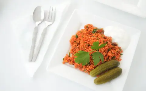 Un plat de boulgour coloré, garni de persil frais, servi avec des cornichons et une touche de yaourt. La cuisson du boulgour est parfaite pour ce repas.