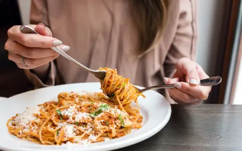 Une personne mange des spaghettis à la sauce tomate et au parmesan avec deux fourchettes.