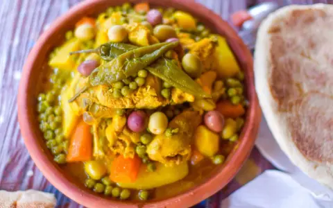 Un plat de tajine poulet aux olives, petits pois et carottes, garni de piments verts. Accompagné de pain.