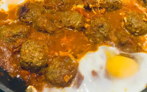 Un plat de tajine kefta oeuf mijote dans une sauce tomate épicée, avec des œufs pochés.