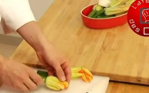 Préparation d'une fleur de courgette recette. Des mains préparent des fleurs de courgette sur une planche à découper.