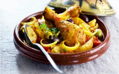 Un plat de tajine poulet citron, avec des morceaux de poulet dorés, des olives, des oignons et des tomates, servi dans un plat en terre cuite.
