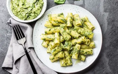 Assiette de pâtes rigatoni généreusement enrobées de pesto vert vif, avec un bol de sauce à côté. Un délice de pâtes au pesto !