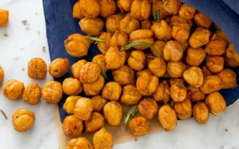 Un tas de pois chiches grillés dorés, certains tombant d'un sac bleu, avec des brins de romarin.