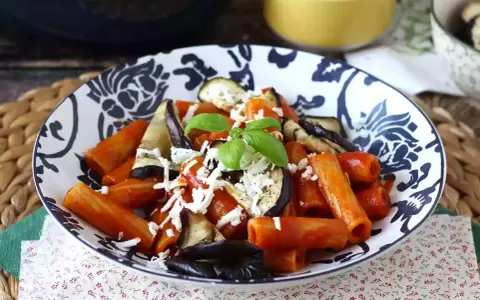 Pâtes rigatoni généreusement garnies de sauce tomate, d'aubergines grillées et de fromage râpé, le tout surmonté d'une feuille de basilic frais. Un plat de pâtes aubergines appétissant.