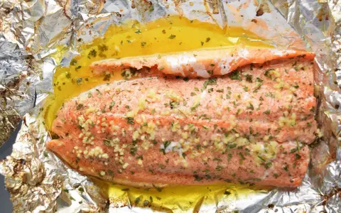 Filet de truite cuit en papillote, assaisonné d'ail et d'herbes, baignant dans un jus doré. Une recette simple et savoureuse.