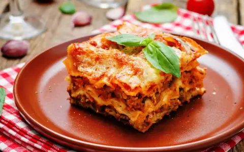 Une part généreuse de lasagne végétarienne, dorée au four, garnie de basilic frais, sur une assiette en terre cuite.