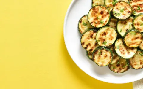 Courgettes rondes grillées à l'air fryer, parsemées d'herbes fraîches, sur une assiette blanche, sur fond jaune vif.