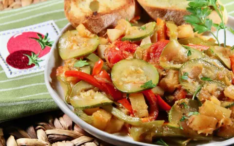 Un plat de légumes mijotés, rappelant un pisto manchego, avec des courgettes, poivrons et tomates, servi avec des toasts grillés.
