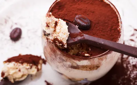 Un déliceux tiramisu cacao, saupoudré de cacao, avec une cuillère pleine de crème onctueuse et un grain de café.