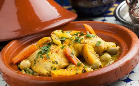 Un plat de tajine recette traditionnelle, avec du poulet, des carottes, des olives et des abricots, garni de persil frais.