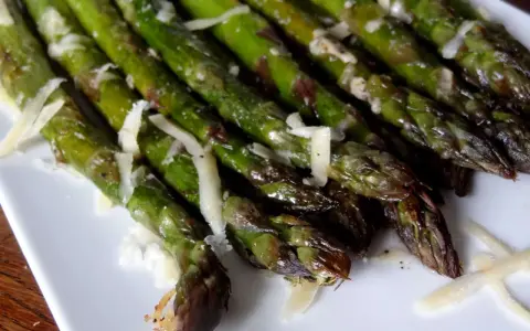 Un plat d'asperges au four, tendres et légèrement grillées, parsemées de copeaux de parmesan. Un délice simple et savoureux.